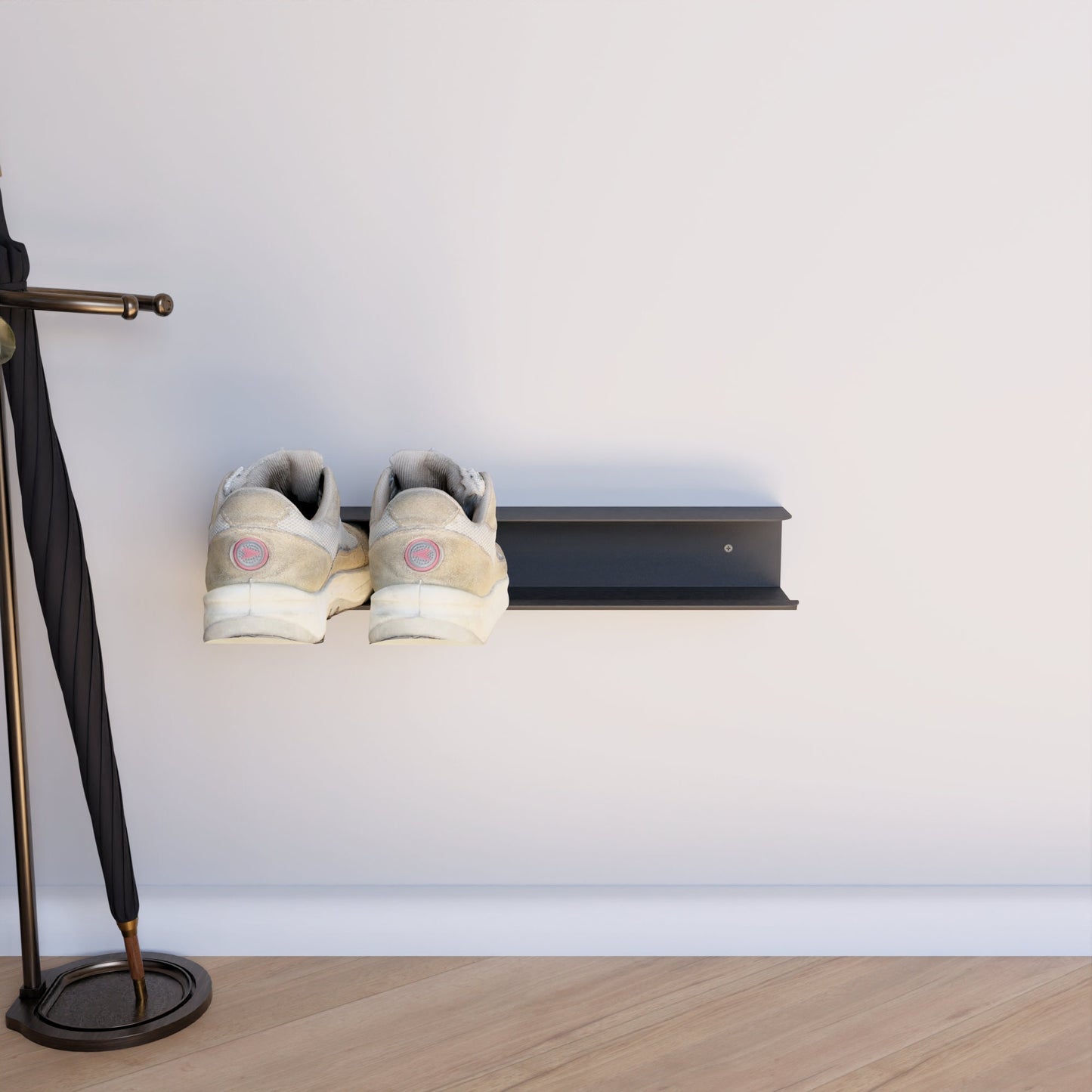 Wall-mounted shoe rack in black, holding a pair of brown patterned sneakers, installed on a white wall next to a potted plant with a wooden floor in the background.